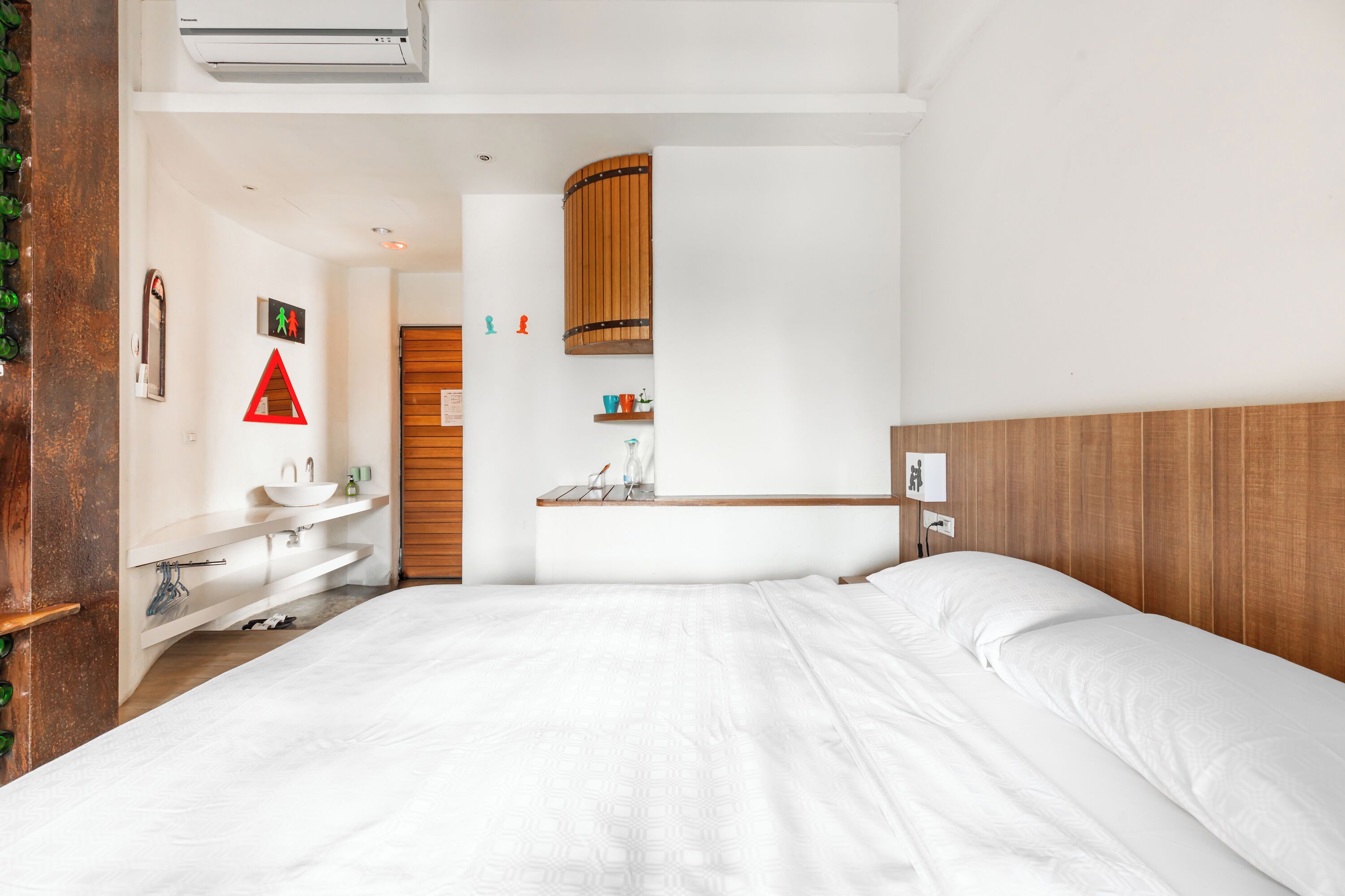 A hotel room with a large bed, a wooden headboard, a white sink, and a small wooden shelf.