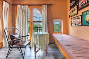 Una habitación con una cama, una mesa con mantel, una silla y una ventana con cortinas.