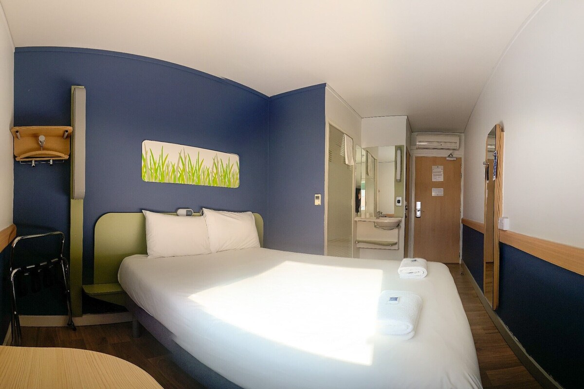 Habitación de hotel con una cama grande, un escritorio, una silla y un baño visible a través de una puerta abierta.