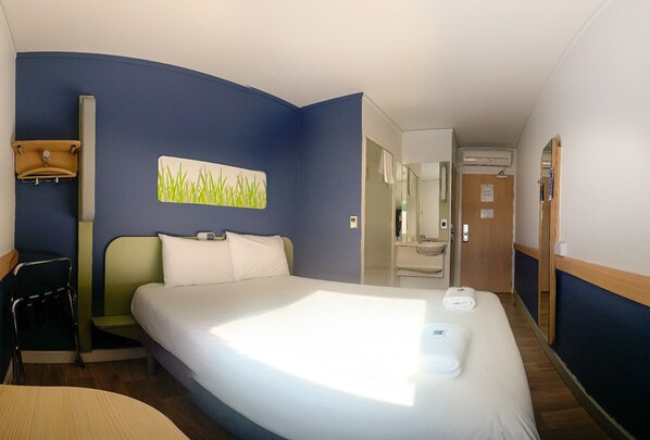 Une chambre d’hôtel avec un grand lit, un bureau, une chaise et une salle de bain visible à travers une porte ouverte.