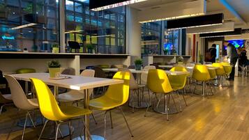A modern dining area with yellow chairs and white tables, large windows, and a view of the cityscape.