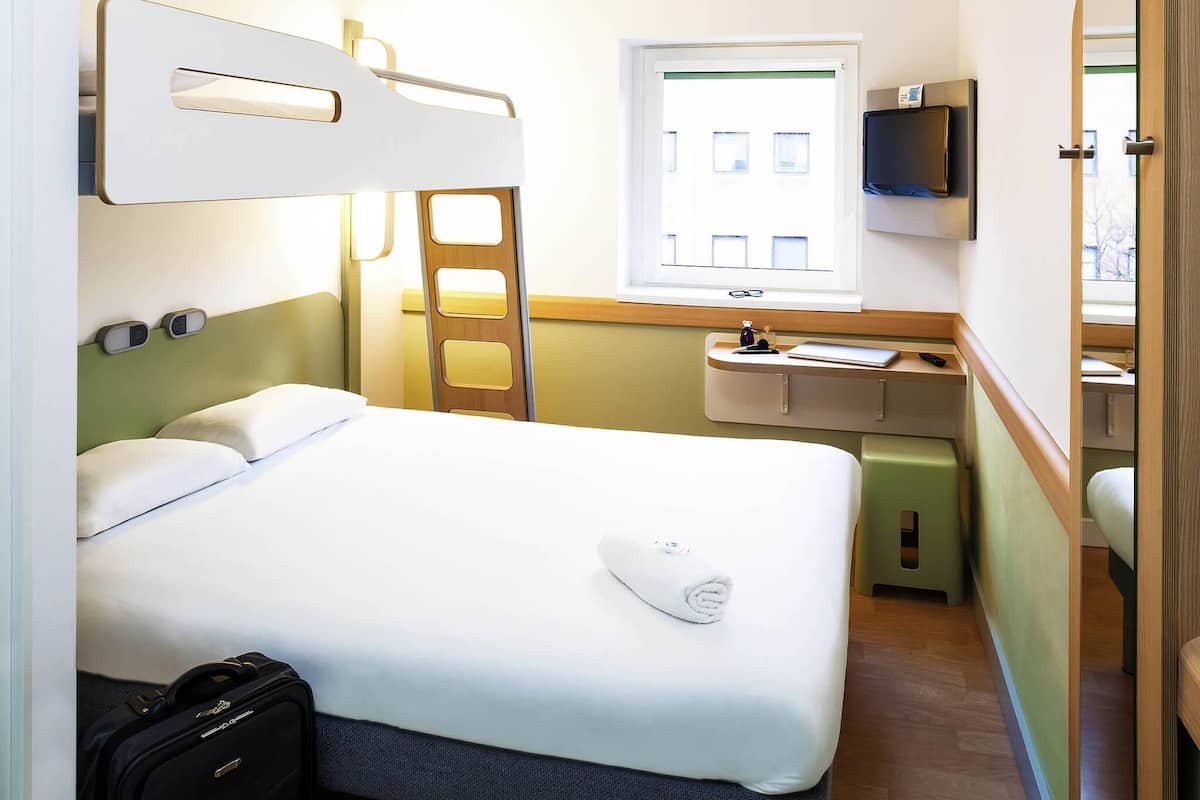 Una habitación de hotel con cama, escritorio, espejo, televisor y ventana.