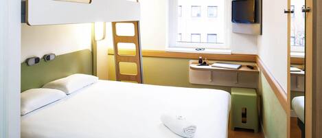 Une chambre d’hôtel avec un lit, un bureau, un miroir, une télévision et une fenêtre.