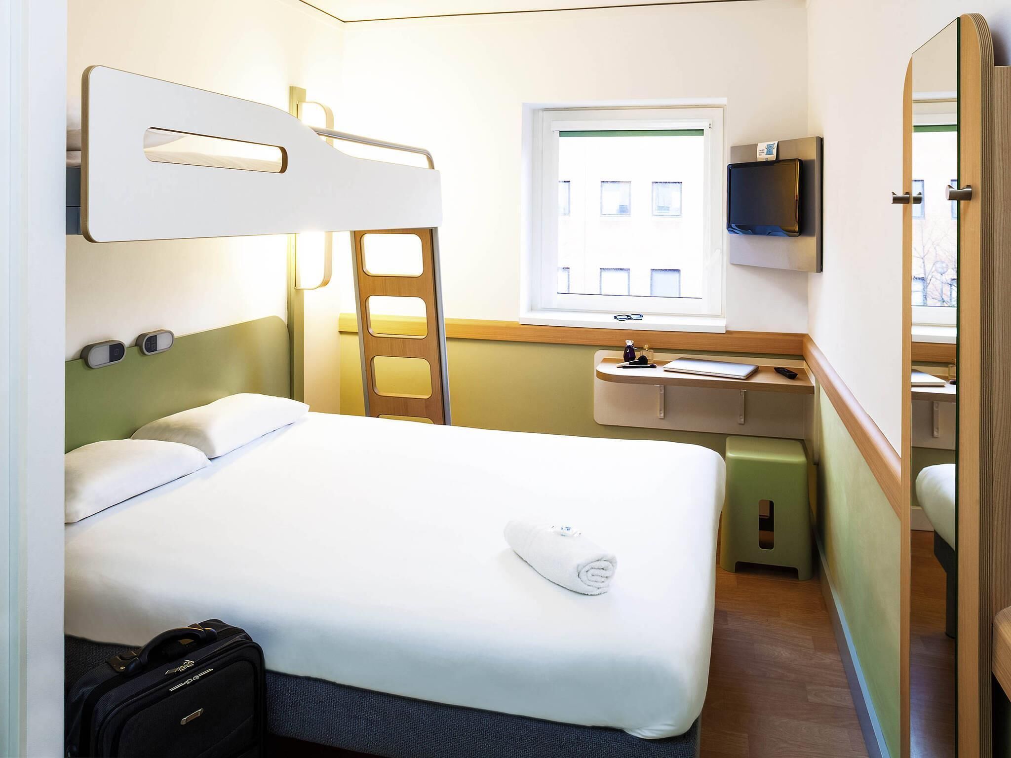 Une chambre d’hôtel avec un lit, un bureau, un miroir, une télévision et une fenêtre.