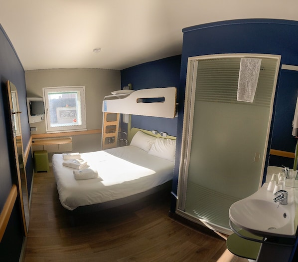 A hotel room with a bed, a bedside table, a mirror, a window, and a bathroom with a sink and toilet. - ibis budget Belfast City Centre (Belfast)