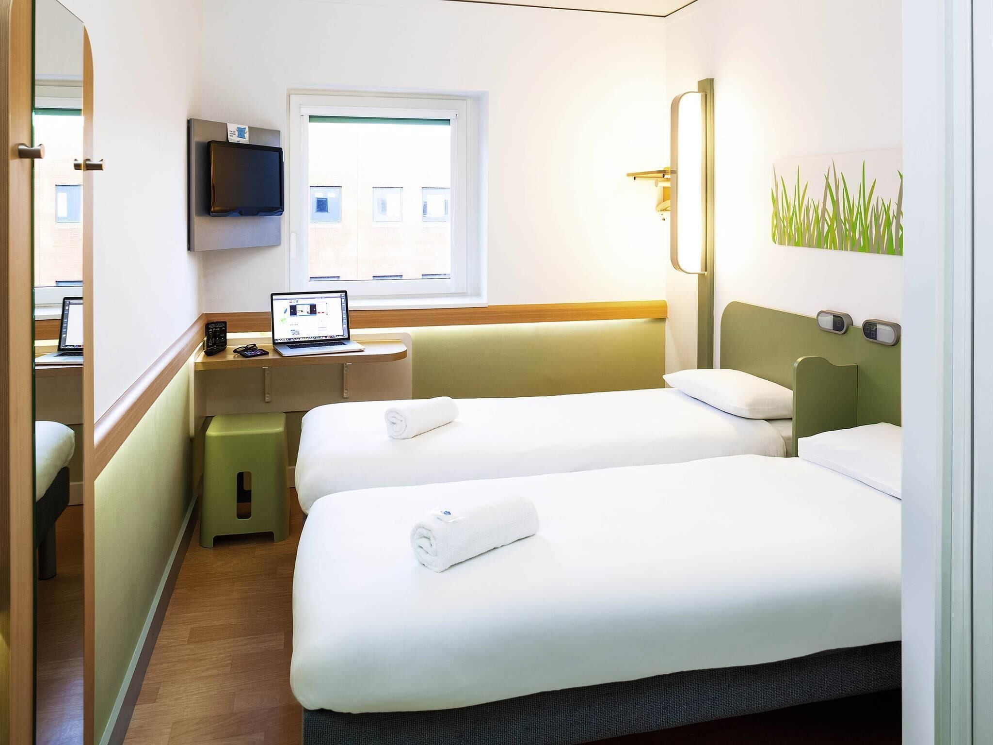 Une chambre d’hôtel avec deux lits, un bureau avec un ordinateur portable, une télévision et une fenêtre.