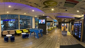Un espacio interior moderno con zonas de estar, una mesa de futbolín y una zona de bar con un letrero de neón.
