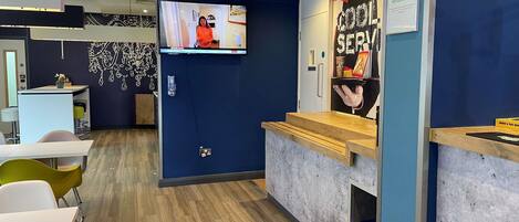 Una zona de recepción moderna con un mostrador de madera, una pantalla de televisión y un cartel que indica alergias e intolerancias alimentarias.