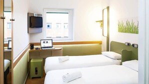 A hotel room with two beds, a desk with a laptop, a television, and a window.