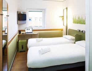 Una habitación de hotel con dos camas, un escritorio con una computadora portátil, un televisor y una ventana.