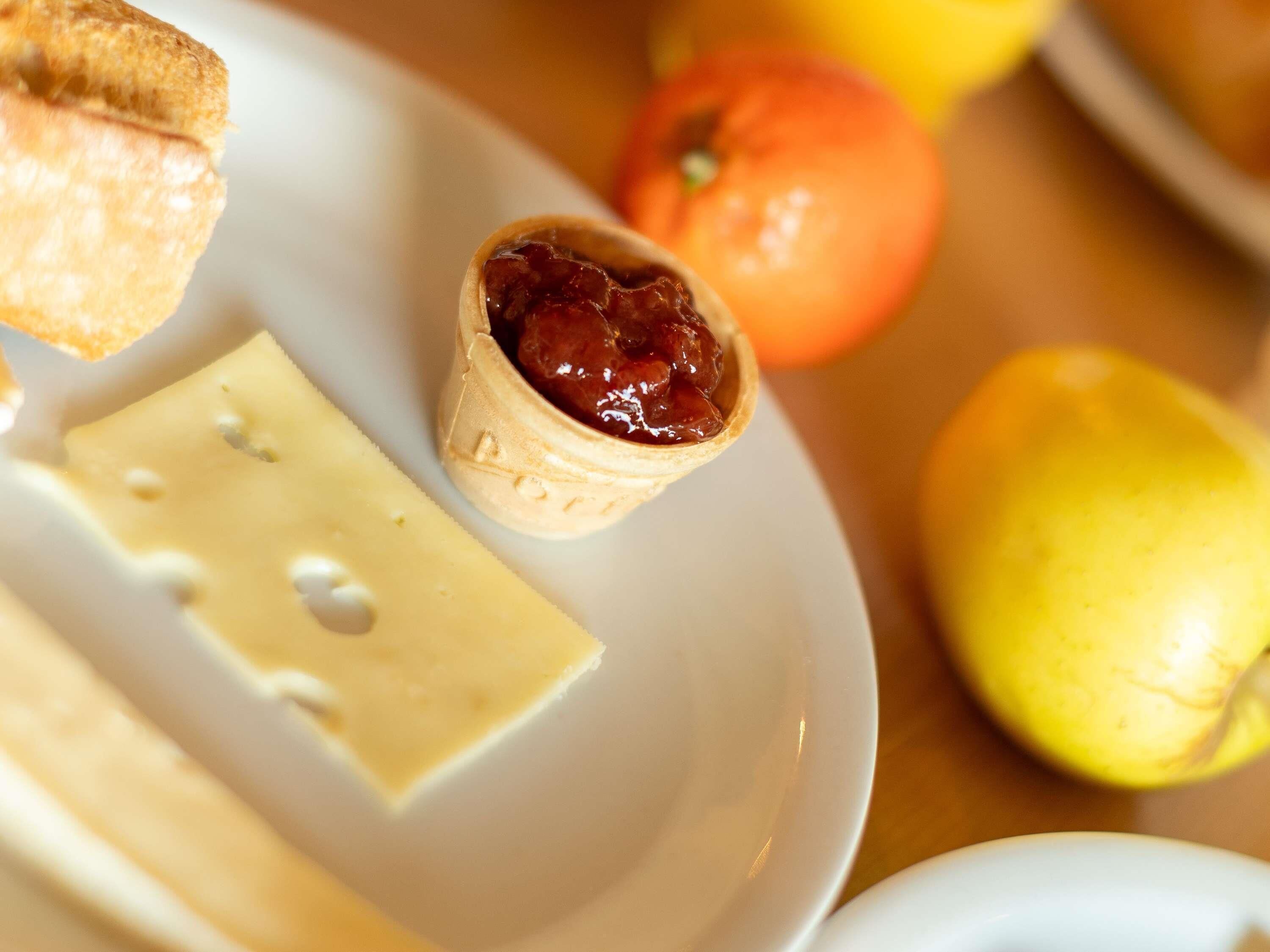 Un plato con un pastel pequeño, una porción de queso y una fruta entera.