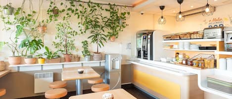 A cafe with a counter, seating area, and various plants.
