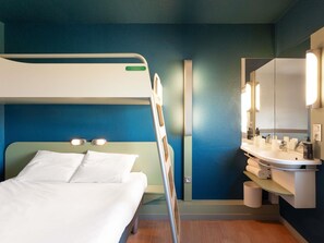 Habitación de hotel con una litera, un baño con lavamanos y espejo, y una pared azul.