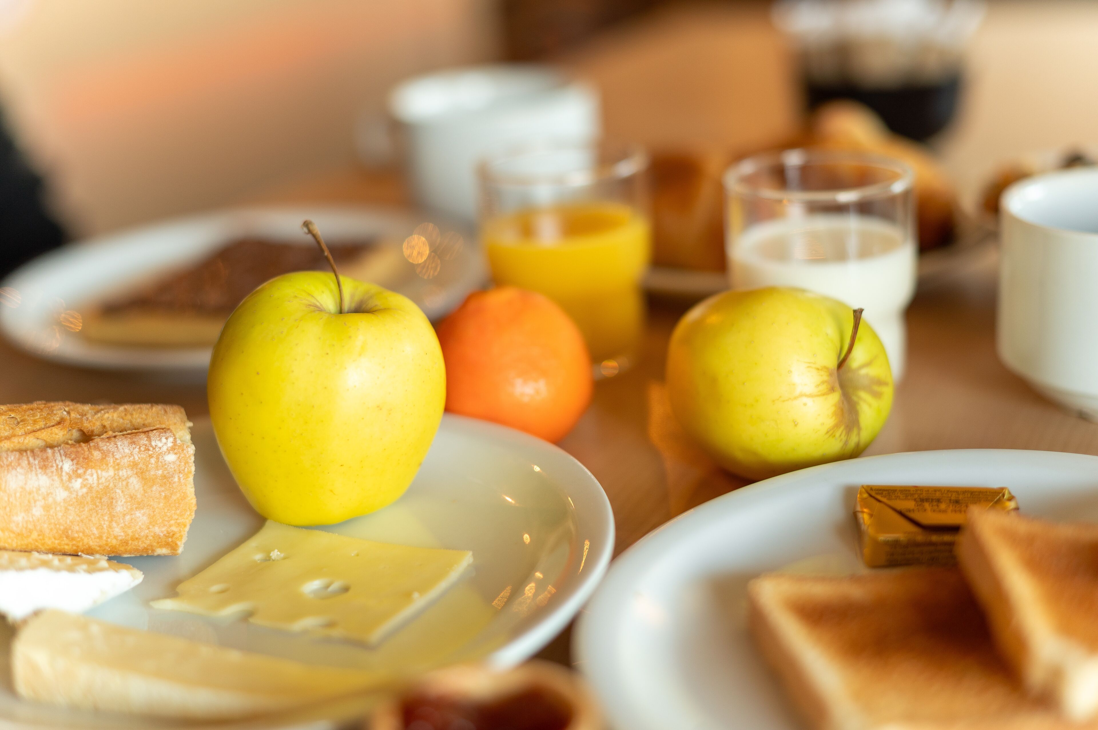 Una escena de desayuno con tostadas, manzanas, una naranja y vasos de zumo de naranja y leche.