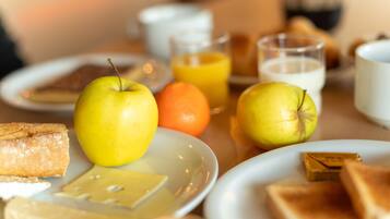 Una escena de desayuno con tostadas, manzanas, una naranja y vasos de zumo de naranja y leche.