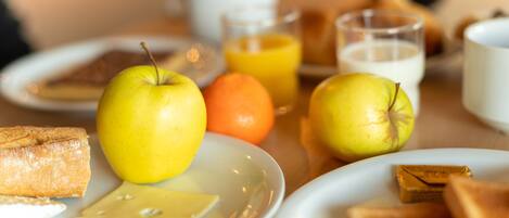 A breakfast setting with plates of toast, apples, an orange, and glasses of orange juice and milk.