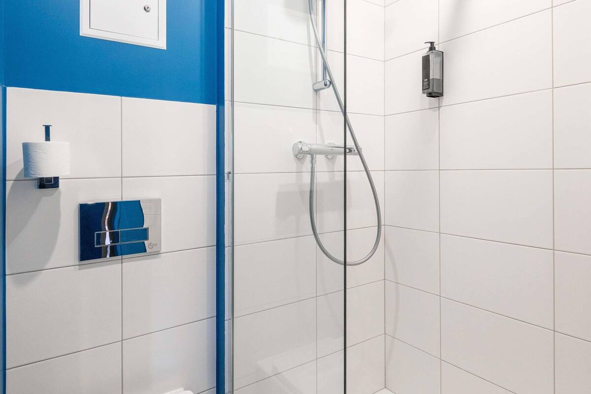 Ein modernes Badezimmer mit weißen Fliesen, einer Duschkabine aus Glas, einer Toilette und einer blauen Akzentwand.