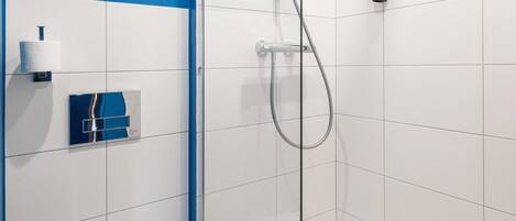 A modern bathroom with white tiles, a glass shower enclosure, a toilet, and a blue accent wall.