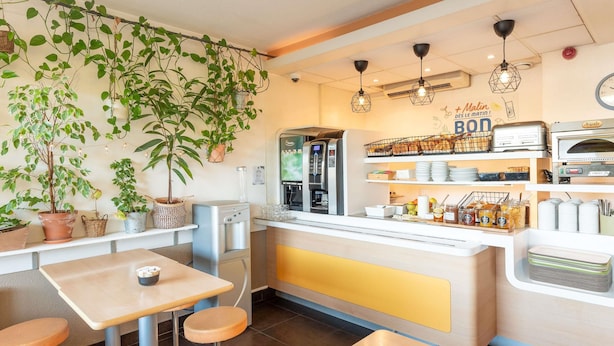 Una cafetería con mostrador, zona de estar y varias plantas.