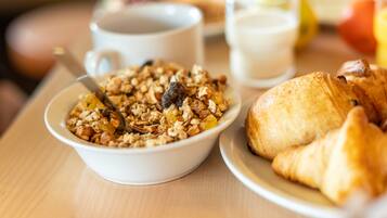 Une table en bois dressée pour le petit-déjeuner, avec un bol de granola, un croissant, une tasse de café et un verre de lait.