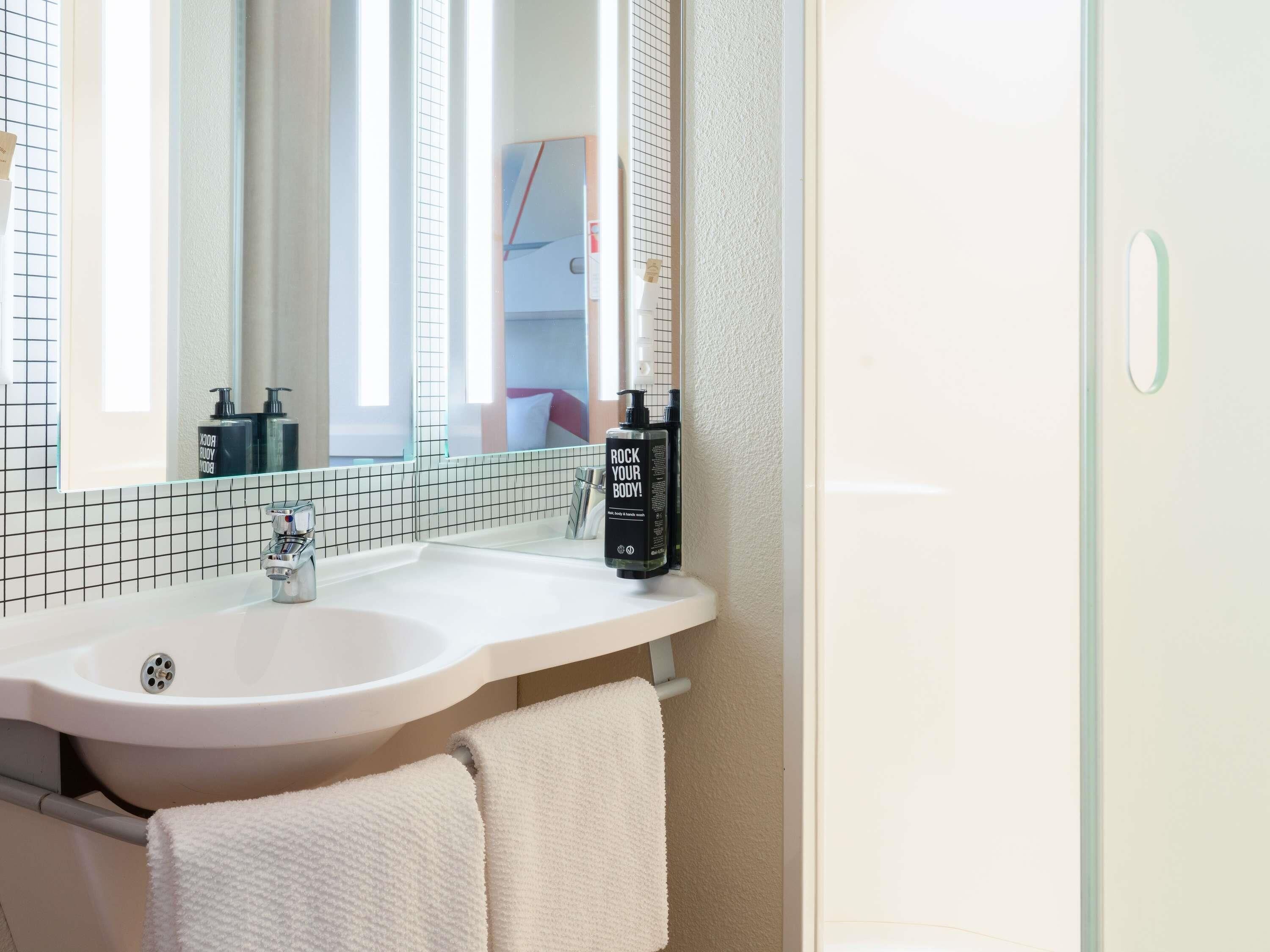 Un baño con un lavamanos blanco, un espejo y dos botellas de loción.