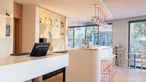 A modern bar area with a white counter, bar stools, and a variety of bottles on shelves. - ibis budget Geneve Petit Lancy (Lancy)
