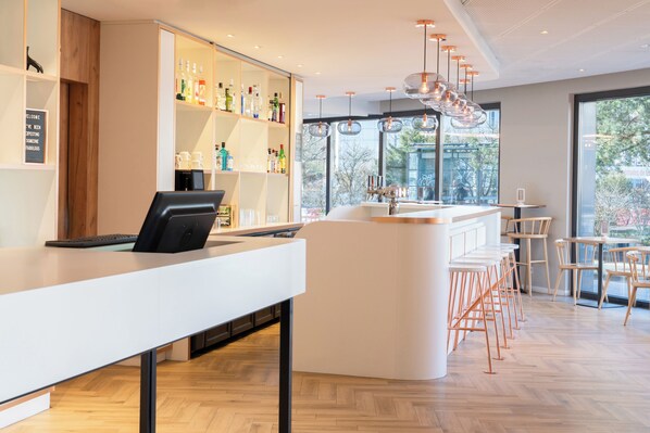 Un área de bar moderna con una barra blanca, taburetes y una variedad de botellas en estanterías.