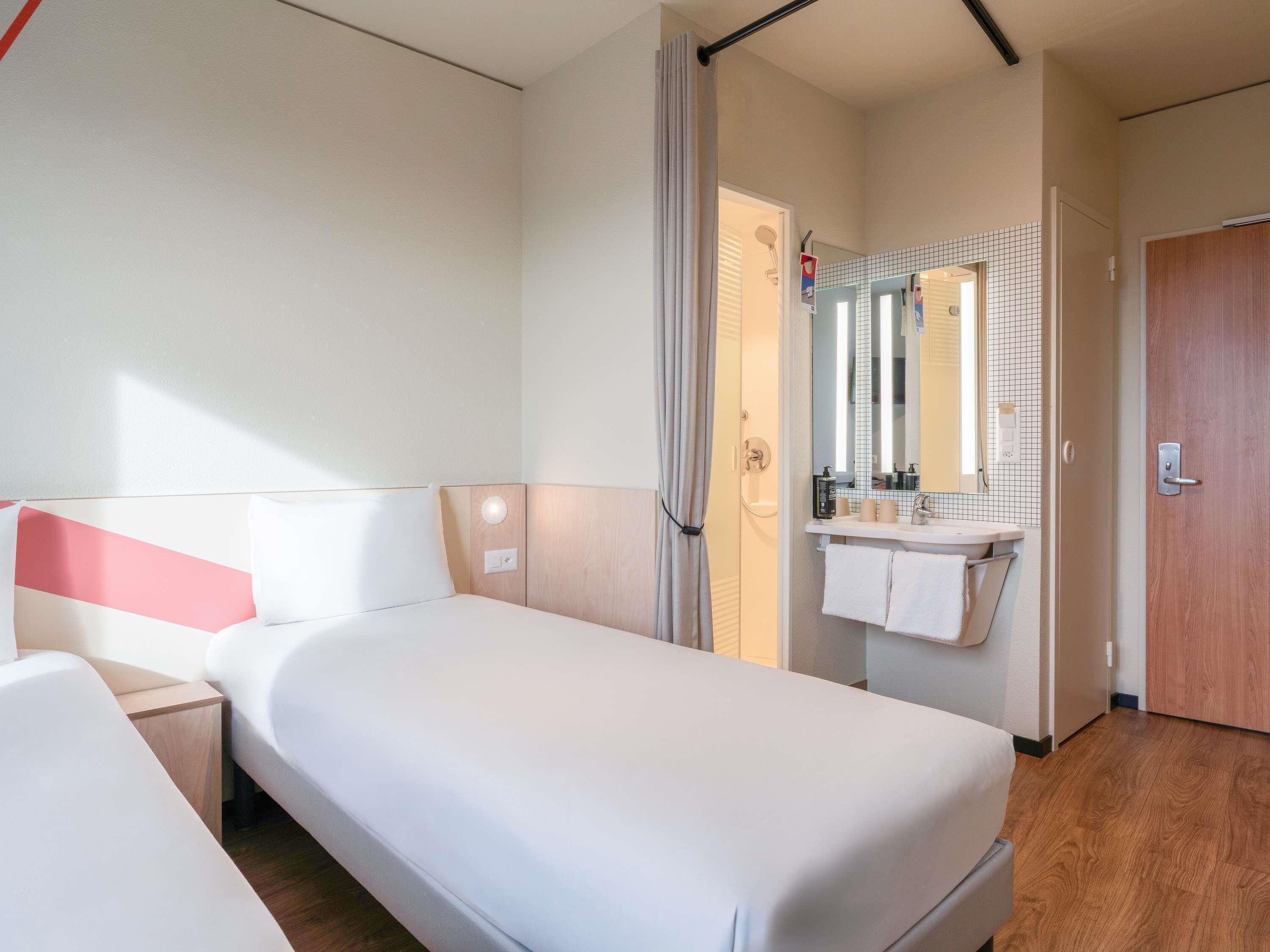 Hotellihuone, jossa on sänky, kylpyhuone peilillä ja pesualtaalla sekä puulattia.