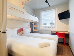 Habitación de hotel con dos camas, un escritorio, una silla, un televisor y una ventana con vista a la ciudad.