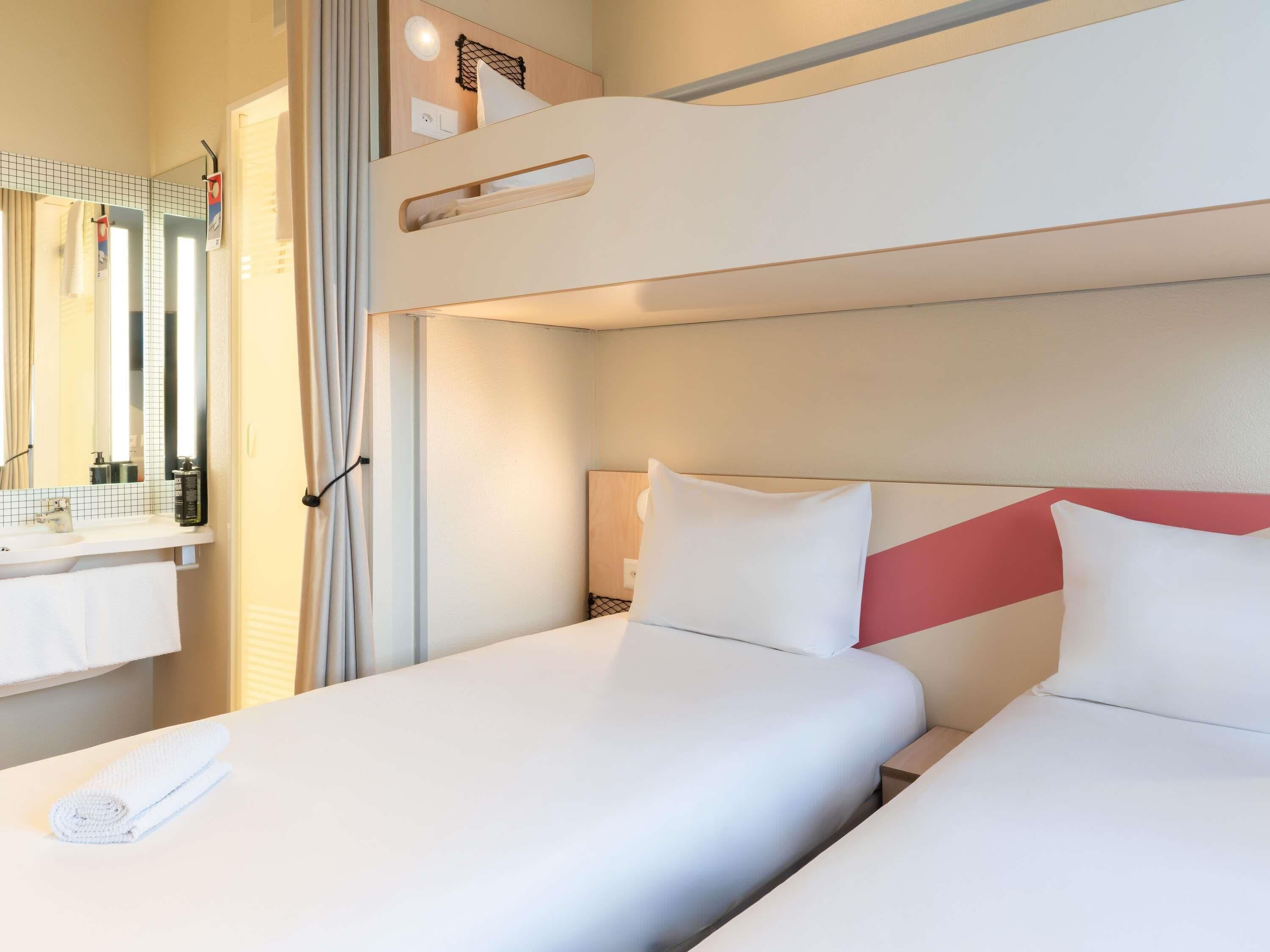 Habitación de hotel con literas, baño con espejo y ventana.