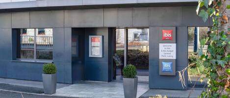 Un edificio moderno con dos letreros para los hoteles ibis e ibis budget. Hay dos plantas en macetas frente a la entrada.