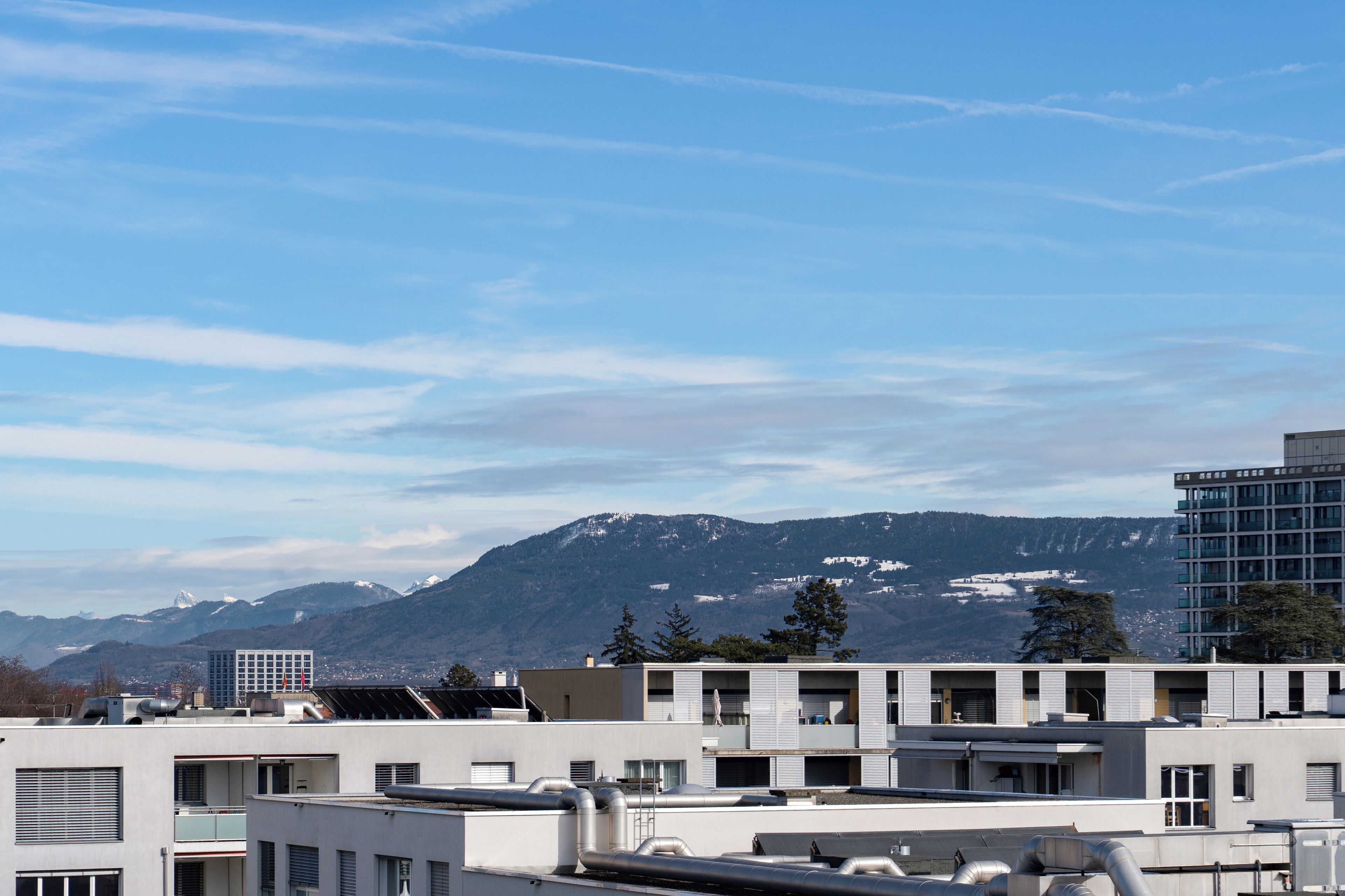 A modern building with multiple floors, large windows, and a flat roof with visible air conditioning units.