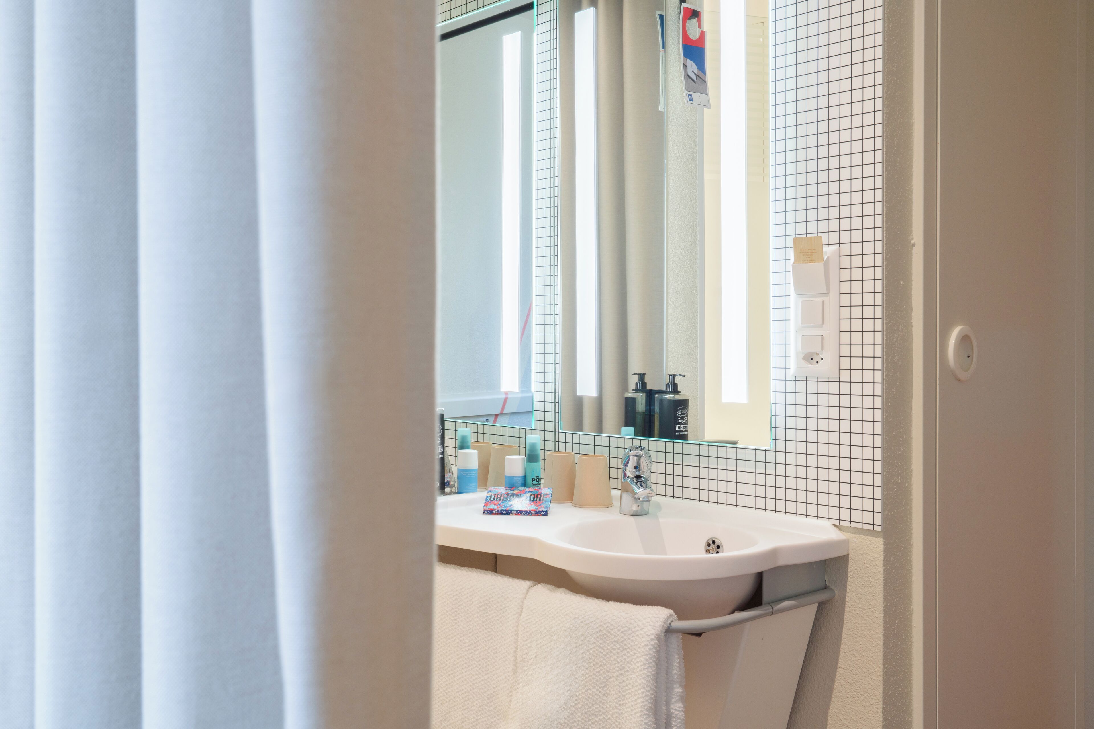 Un baño con lavamanos blanco, espejo y paredes con azulejos.
