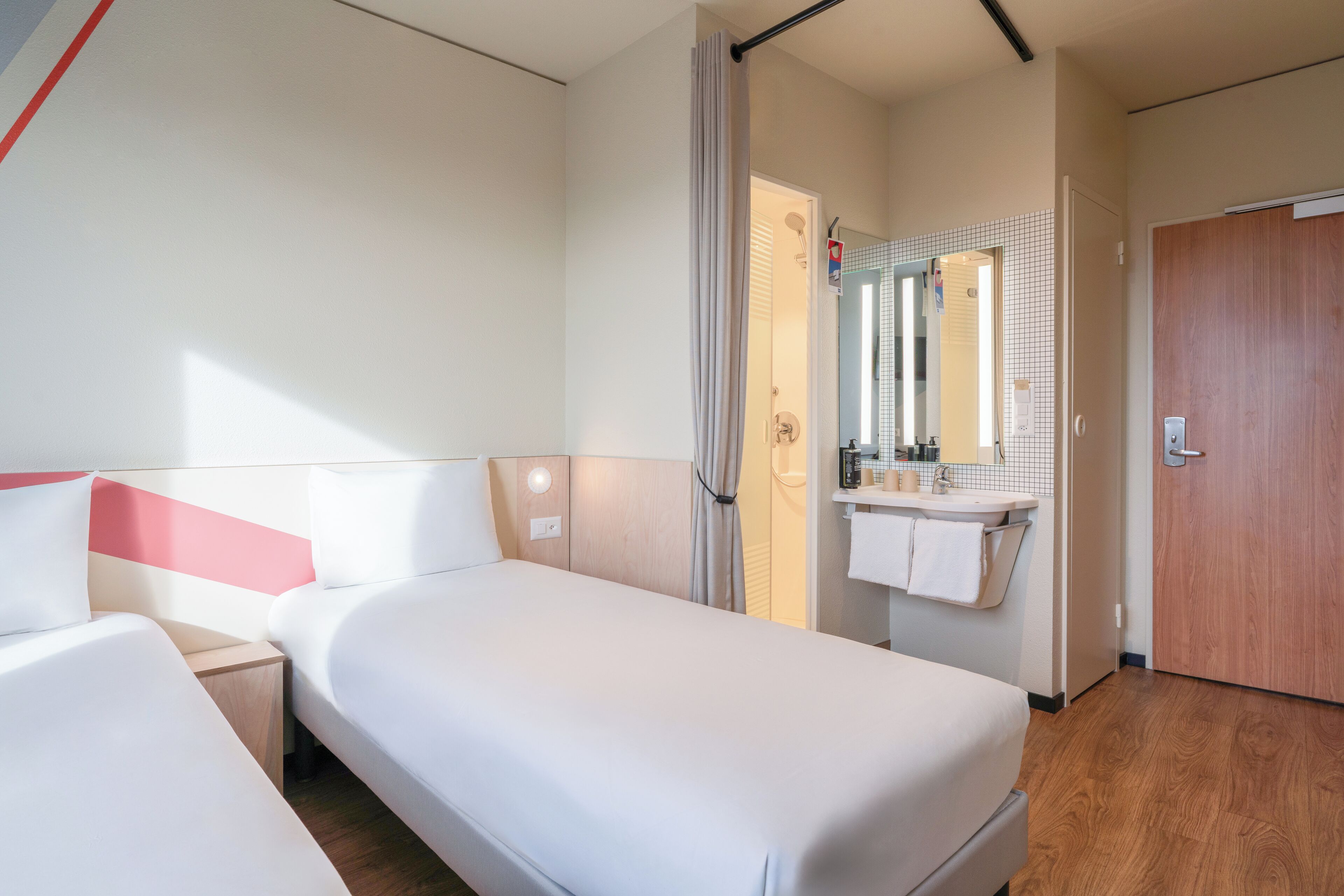 Une chambre d’hôtel avec deux lits, une salle de bain avec un miroir et un plancher en bois.