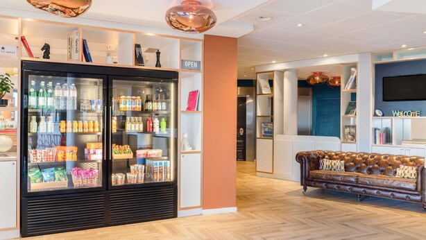 Een moderne hotellobby met een grote drankkoeler, een leren bank en een receptiebalie.