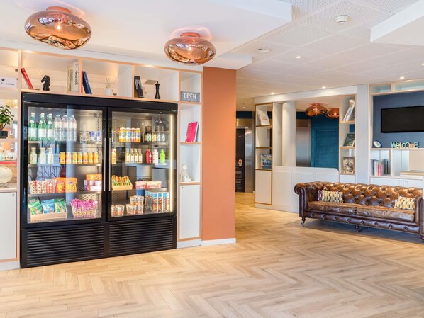 A modern hotel lobby with a large beverage refrigerator, a leather sofa, and a reception desk. - ibis budget Geneve Petit Lancy (Lancy)