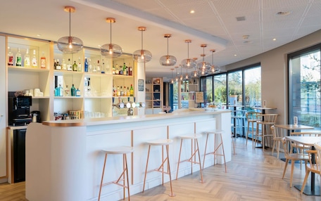 A modern bar area with a white counter, multiple stools, and a variety of bottles and glasses on shelves.