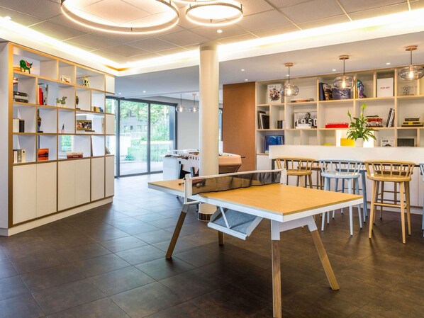 A modern interior with a dining area, bookshelves, and a view through large windows. - ibis budget Geneve Petit Lancy (Lancy)