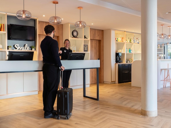 Un hall d’hôtel moderne avec un comptoir d’accueil, un bar et une horloge murale.