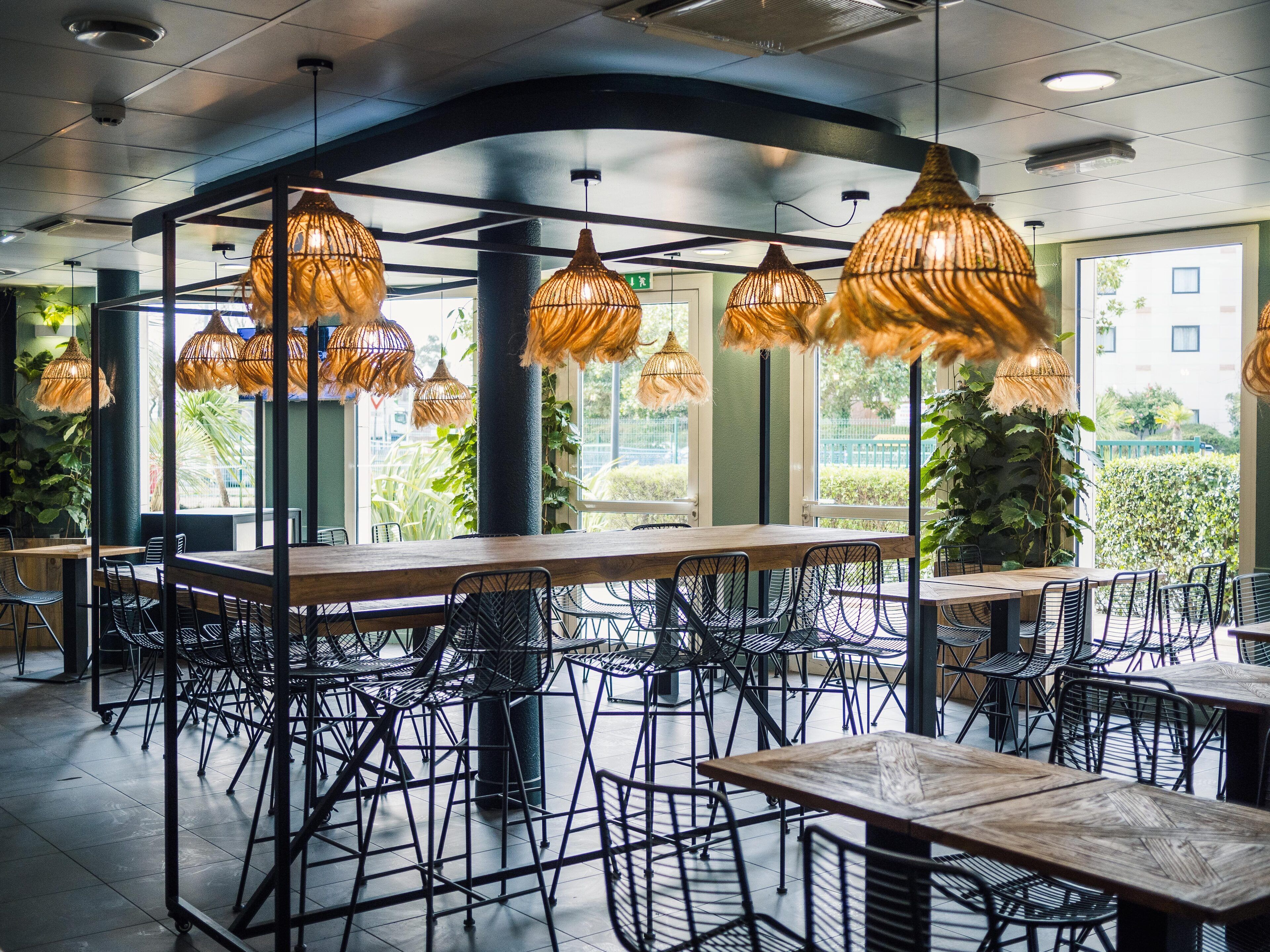 A restaurant interior with high tables and chairs, large windows, and hanging wicker lamps.