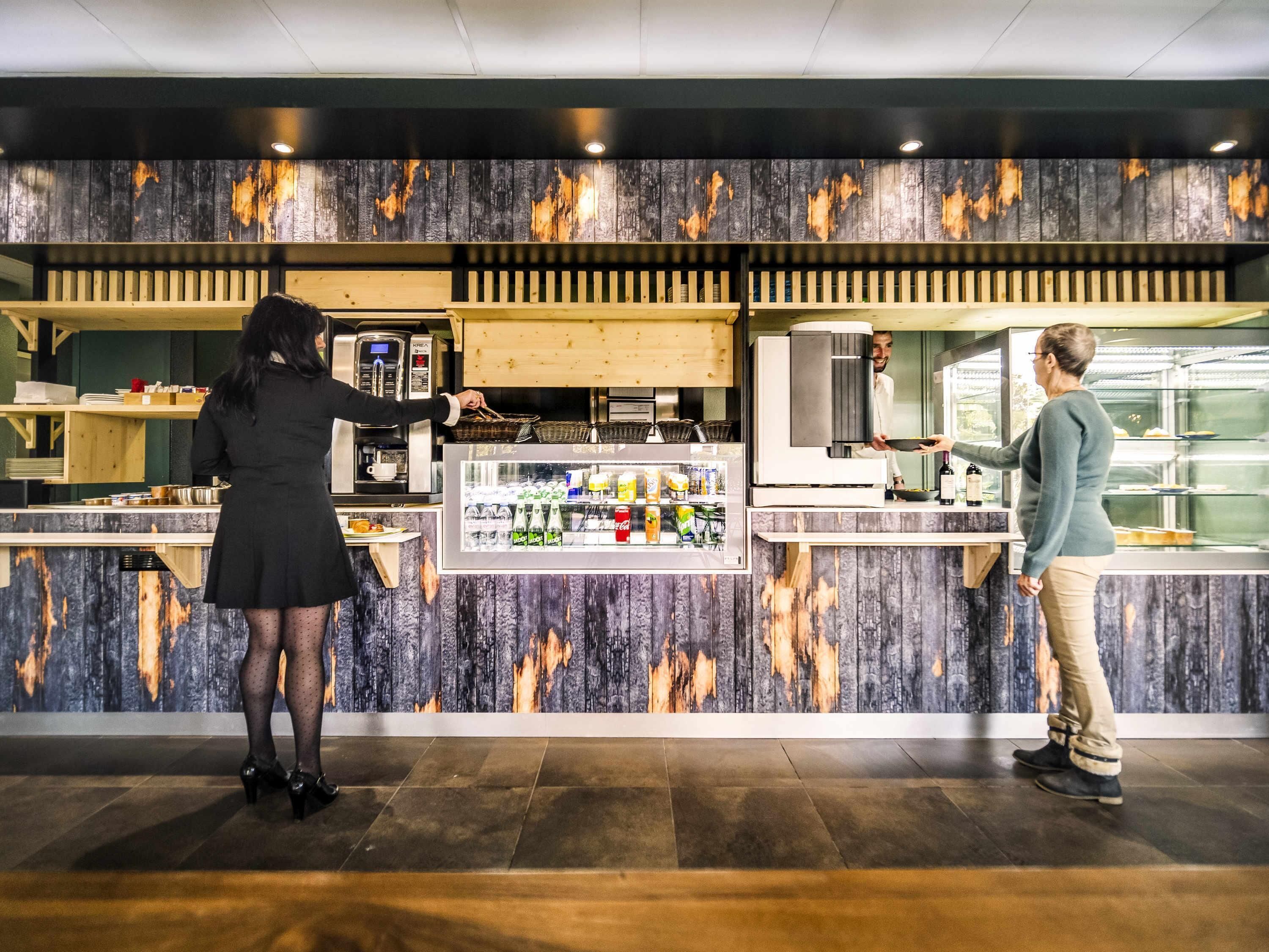 Un comptoir équipé d’une machine à café, d’un réfrigérateur-vitrine et d’une personne qui sert un client.