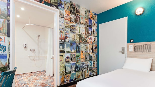 A hotel room with a bed, a shower, and a wall decorated with travel posters.