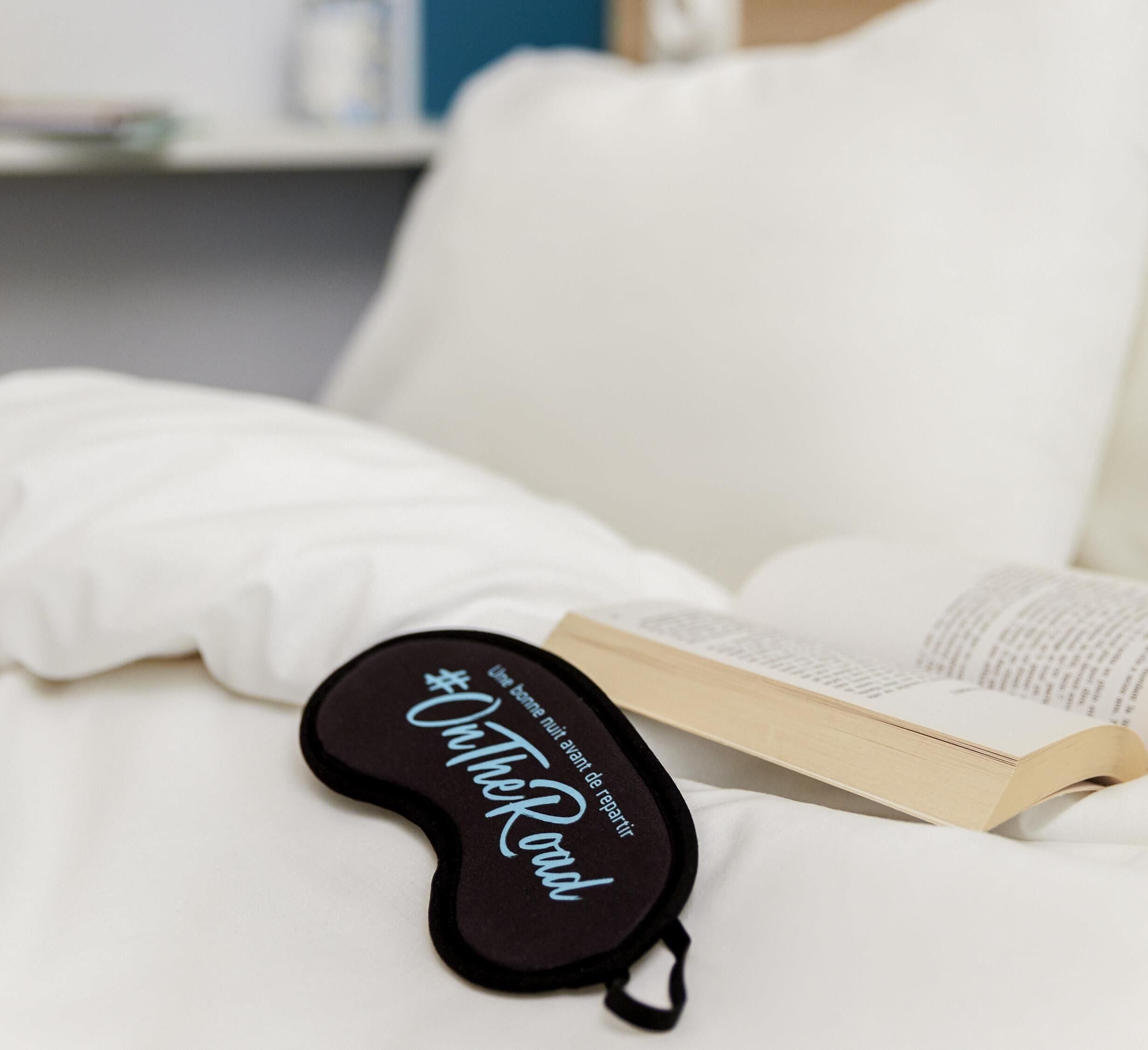 A book on a white bed with a black pillow with text on it.