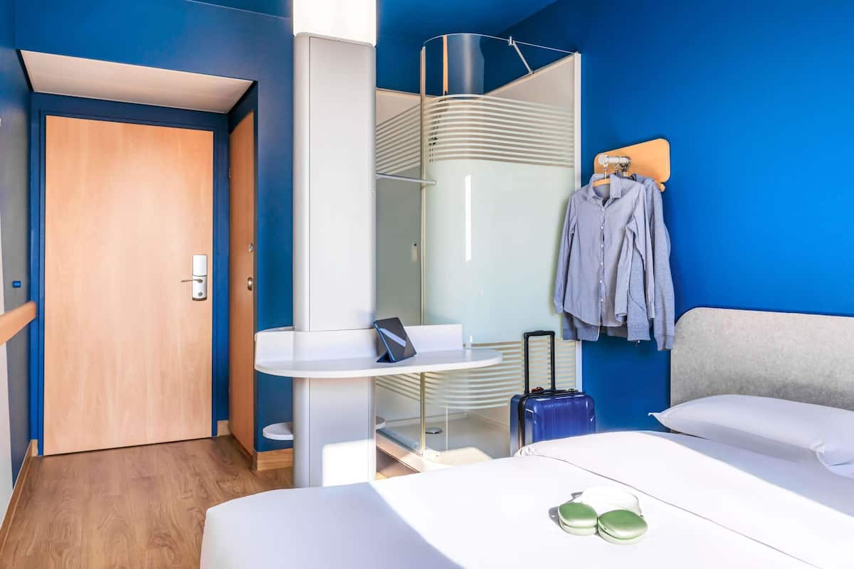 A modern hotel room with a bed, a desk, a wardrobe, and a hanging clothes rack.