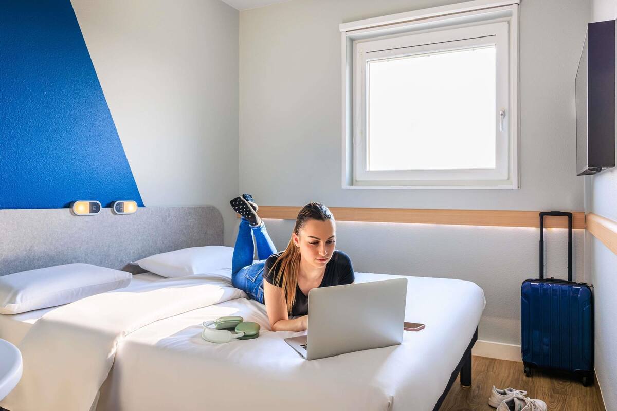 A hotel room with a bed, a laptop, a suitcase, and a TV on the wall.