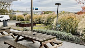 A covered picnic area with wooden benches and a view of a road and buildings in the background.