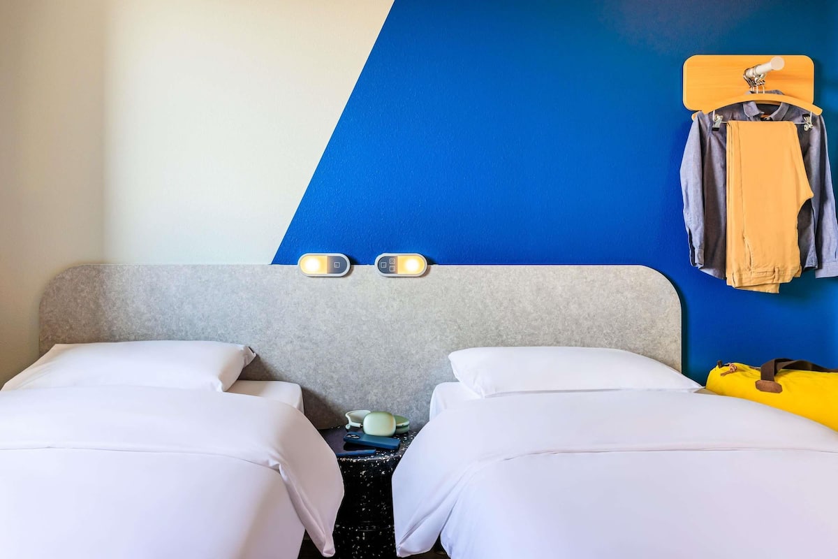 A hotel room with two beds, a blue wall, and a wooden headboard.