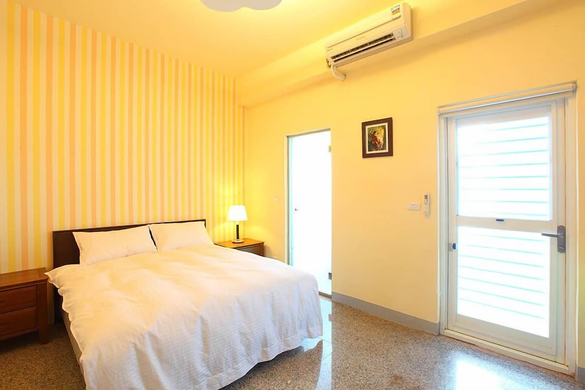 Una habitación de hotel con cama, mesita de noche, lámpara, puerta y equipo de aire acondicionado.