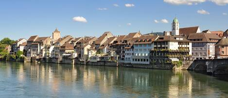 A riverside town with historic buildings, a prominent tower, and a bridge.
