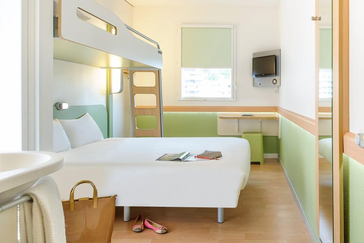 Une chambre d’hôtel avec un lit superposé, un bureau, une télévision et une fenêtre.